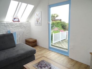 A room with a gray couch a wicker basket a small white gate and a door with a blue frame leading outside at Anchorage in Watchet