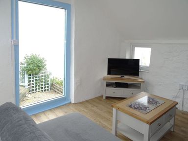 A small living room with a TV on a stand a coffee table a sofa and a large window with blue trim at Anchorage in Watchet