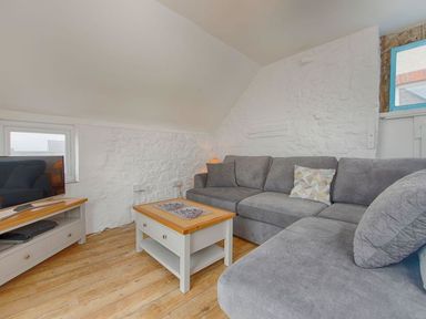 A living room with grey sofa a wooden coffee table television on a stand and stone walls at Anchorage in Watchet