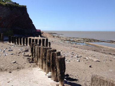A sandy beach with wooden posts in a row near a rocky cliff and the sea at Anchorage in Watchet