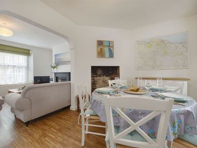 A dining area with a round table set with plates and glasses next to a sitting area with sofas and a television at Anchorage in Watchet