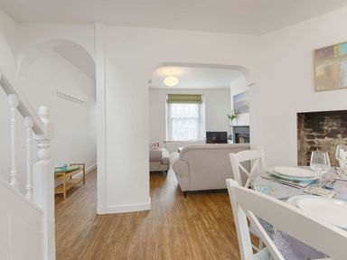 A dining area with a table set for four and a view into a living room with sofas and a window at Anchorage in Watchet