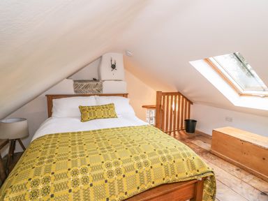 A bedroom with a wooden bed with yellow patterned bedding a bedside lamp a wooden chest and a skylight window at Bwthyn Lan in Boncath