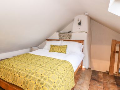 A bedroom with a wooden bed with white sheets and a yellow patterned blanket under a sloped ceiling at Bwthyn Lan in Boncath
