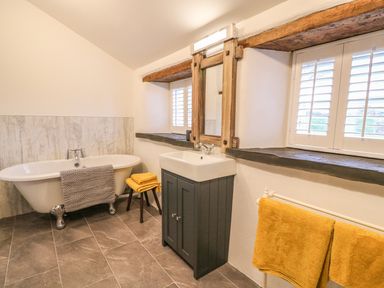 A bathroom with a clawfoot bathtub gray towel yellow towels sink under a mirror and window shutters at Bwthyn Lan in Boncath