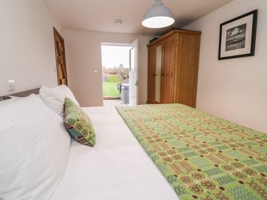 A bedroom with a bed covered with a green patterned quilt a wooden wardrobe a framed picture on the wall and an open door leading outside at Bwthyn Lan in Boncath