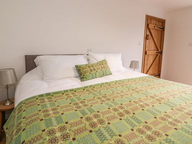 A bedroom with a bed covered with a patterned green blanket and pillows two bedside lamps and a wooden door at Bwthyn Lan in Boncath