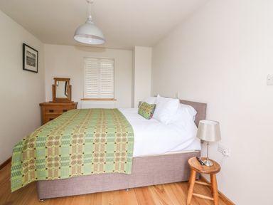 A bedroom with a bed covered with a green patterned blanket a wooden dresser with a mirror and a small wooden stool with a lamp at Bwthyn Lan in Boncath