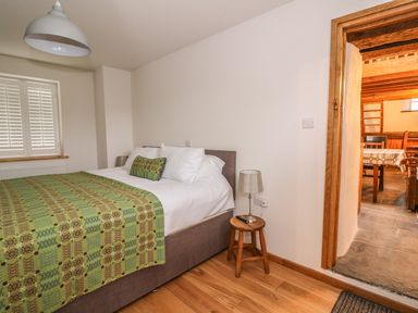 A bedroom with a bed covered with a green patterned blanket and pillows with a stool serving as a bedside table with a lamp and remote at Bwthyn Lan in Boncath