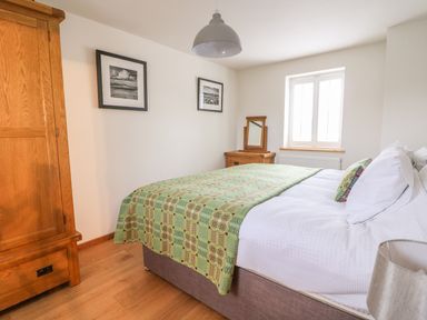 A bedroom with a bed covered with a green patterned blanket a wooden wardrobe a dressing table and framed pictures on the wall at Bwthyn Lan in Boncath