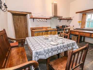 A kitchen with wooden table and chairs a stove and shelves with glassware at Bwthyn Lan in Boncath