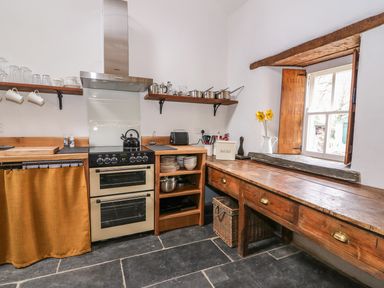 A kitchen with an oven stove wooden shelves pots a window and a wooden countertop at Bwthyn Lan in Boncath