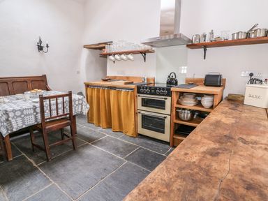 A kitchen with a stove wooden shelves and a table with chairs at Bwthyn Lan in Boncath