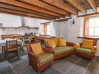 A kitchen and living area with wooden beams on the ceiling a table with chairs and leather armchairs at Bwthyn Lan in Boncath