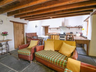 A living area with a sofa and armchair facing a dining table and a kitchen with wooden beams at Bwthyn Lan in Boncath