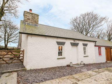 An exterior view of a white cottage with a slate roof a stone chimney two windows and a wooden gate at Bwthyn Lan in Boncath