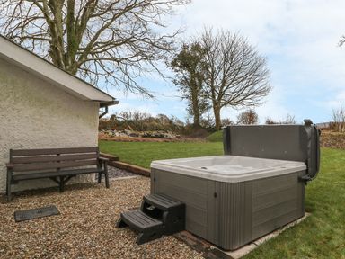 An outdoor area with a hot tub and a wooden bench on a gravel surface at Bwthyn Lan in Boncath