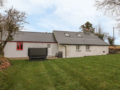 An exterior view of a single story house with a grey tiled roof two skylights and a green lawn at Bwthyn Lan in Boncath
