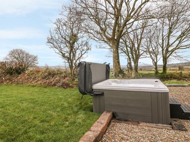 A hot tub with an open cover on a gravel and grass area with trees and fields in the background at Bwthyn Lan in Boncath