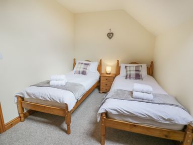 A bedroom with two single wooden beds a nightstand with a lamp and folded towels at Pentrego Isaf in Meifod