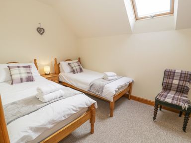 A bedroom with two single beds a wooden nightstand a chair and a skylight window at Pentrego Isaf in Meifod