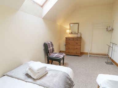 A bedroom with a bed, chair, wooden chest of drawers with a lamp and mirror, and a clothes rack at Pentrego Isaf in Meifod