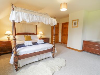 A bedroom with a four poster bed bedside tables lamps dressers and a rug at Pentrego Isaf in Meifod