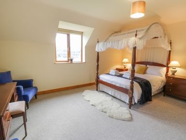 A bedroom with a four poster bed bedside tables and lamps a blue armchair a desk and chair at Pentrego Isaf in Meifod