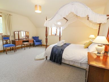 A bedroom with a canopy bed a dresser with mirror two chairs and lamps at Pentrego Isaf in Meifod