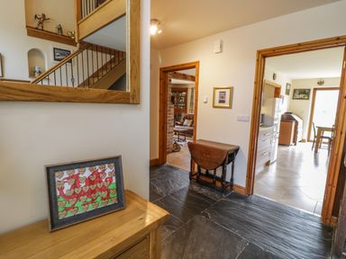 A hallway with stone flooring wooden furniture and views into a living room and kitchen at Pentrego Isaf in Meifod