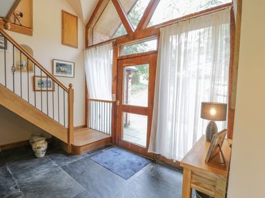 An entryway with a wooden staircase door with glass panels a wooden table with a lamp and framed photo and a blue doormat at Pentrego Isaf in Meifod