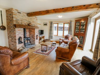A living room with leather armchairs a wooden coffee table a brick fireplace and a wooden cabinet at Pentrego Isaf in Meifod