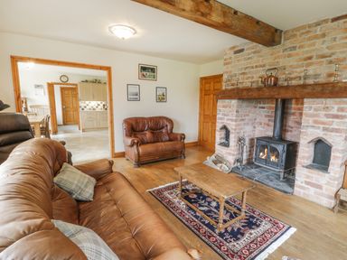 A living room with brown leather sofas wood flooring a wooden coffee table a rug and a brick fireplace with a wood stove at Pentrego Isaf in Meifod