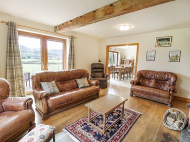 A living room with leather sofas a wooden coffee table and a rug with dining area in the background at Pentrego Isaf in Meifod