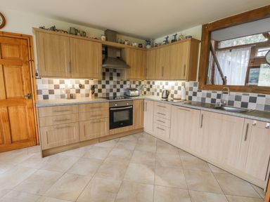 A kitchen with wooden cabinets a tiled floor a built in oven and sink at Pentrego Isaf in Meifod