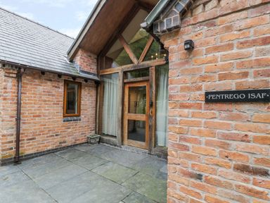 An exterior brick entrance with a wooden door and large windows at Pentrego Isaf in Meifod