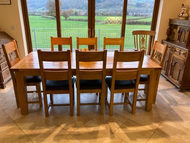 A dining room with a wooden table and eight chairs near large windows showing a green field at Pentrego Isaf in Meifod