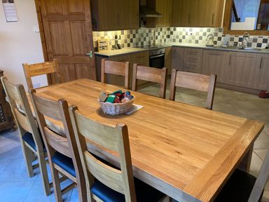 A kitchen with wooden cabinets a dining table with six chairs and a basket on the table at Pentrego Isaf in Meifod