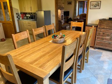 A dining area with a wooden table and eight chairs next to a kitchen with cabinets and appliances at Pentrego Isaf in Meifod