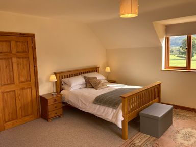 A bedroom with a wooden bed white bedding bedside tables with lamps a window with a view and a grey storage bench at Pentrego Isaf in Meifod