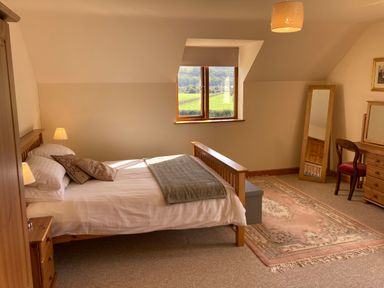 A bedroom with a bed desk chair rug and window showing a countryside view at Pentrego Isaf in Meifod