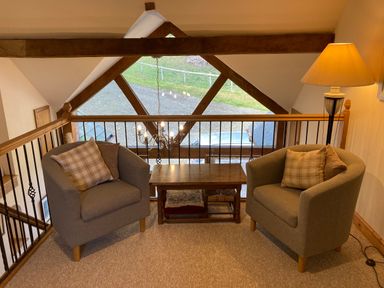 A seating area with two armchairs a wooden coffee table and a floor lamp by a railing with a window showing outdoors at Pentrego Isaf in Meifod