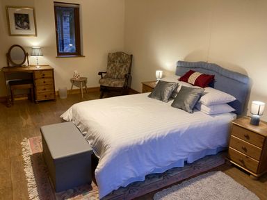 A bedroom with a bed and pillows bedside tables with lamps a chair a wooden dressing table with a lamp and mirror and a small bench at Pentrego Isaf in Meifod