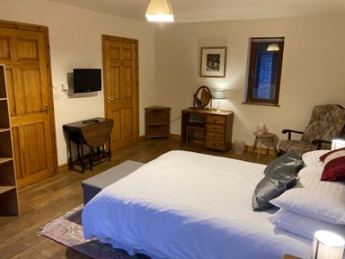 A bedroom with a bed pillows armchair dressing table and television at Pentrego Isaf in Meifod