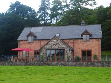 A two story brick and stone house with a slate roof and outdoor furniture on a patio at Pentrego Isaf in Meifod