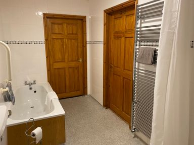 A bathroom with a bathtub wooden doors a metal towel rail and a shower curtain at Pentrego Isaf in Meifod