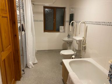 A bathroom with a bathtub a toilet a sink a shower curtain a towel rack and a window at Pentrego Isaf in Meifod