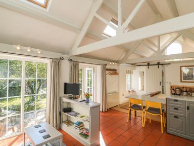 A living area with skylights a bookshelf a small dining table with two yellow chairs and sliding glass doors at The Daffodil Shed in Bere Alston