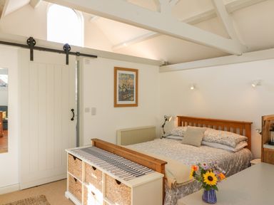 A bedroom with a wooden bed, a sliding door, a chest with baskets, and a vase with flowers at The Daffodil Shed in Bere Alston
