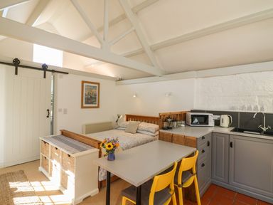 A studio room with a bed kitchen area with microwave and kettle yellow chairs and a small table at The Daffodil Shed in Bere Alston
